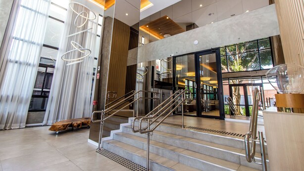 Eine moderne Hotelhalle mit Treppe, großen Fenstern und einer hölzernen Bank.