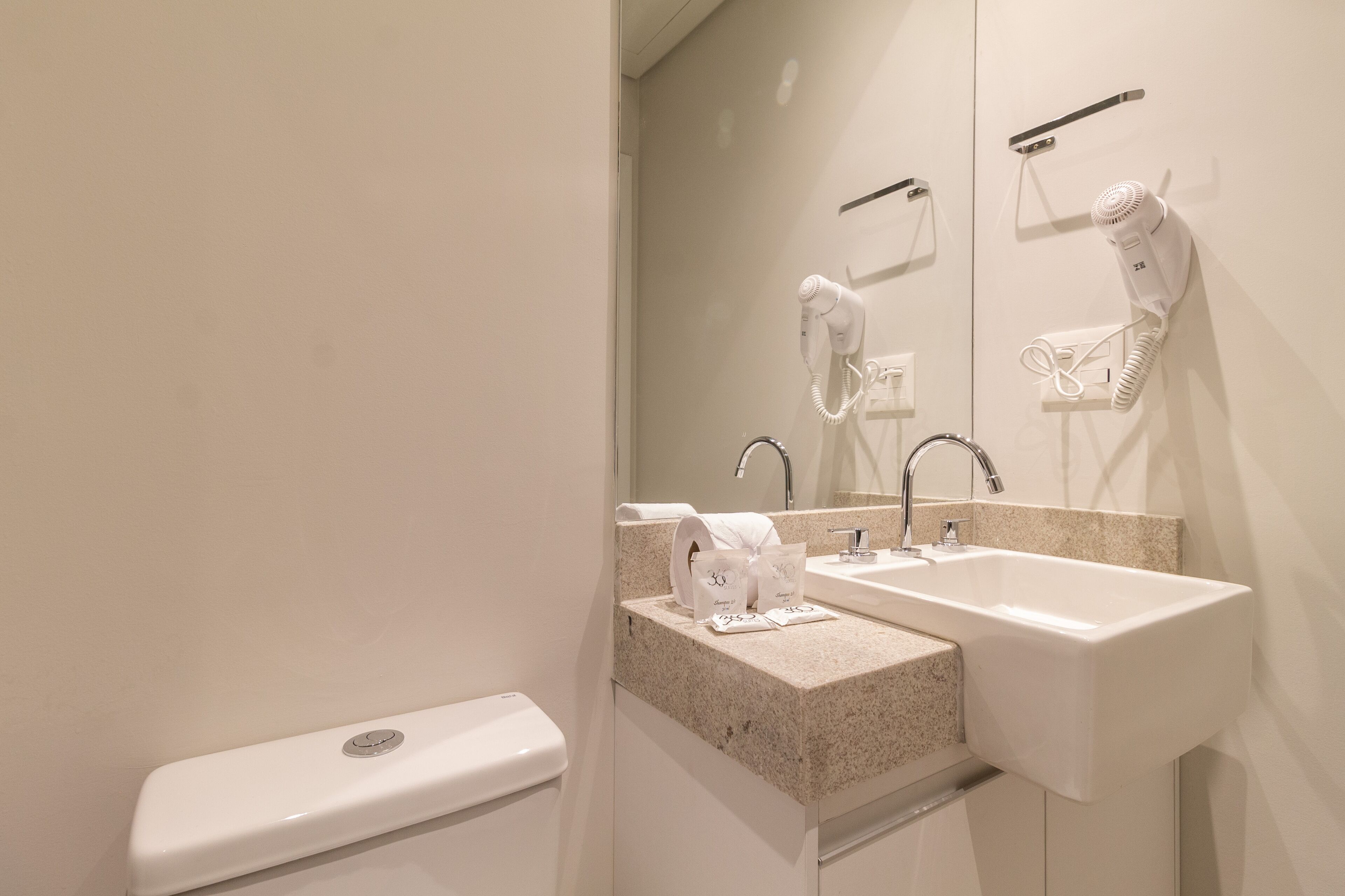 A modern bathroom with a double sink, a toilet, and a hairdryer mounted on the wall.