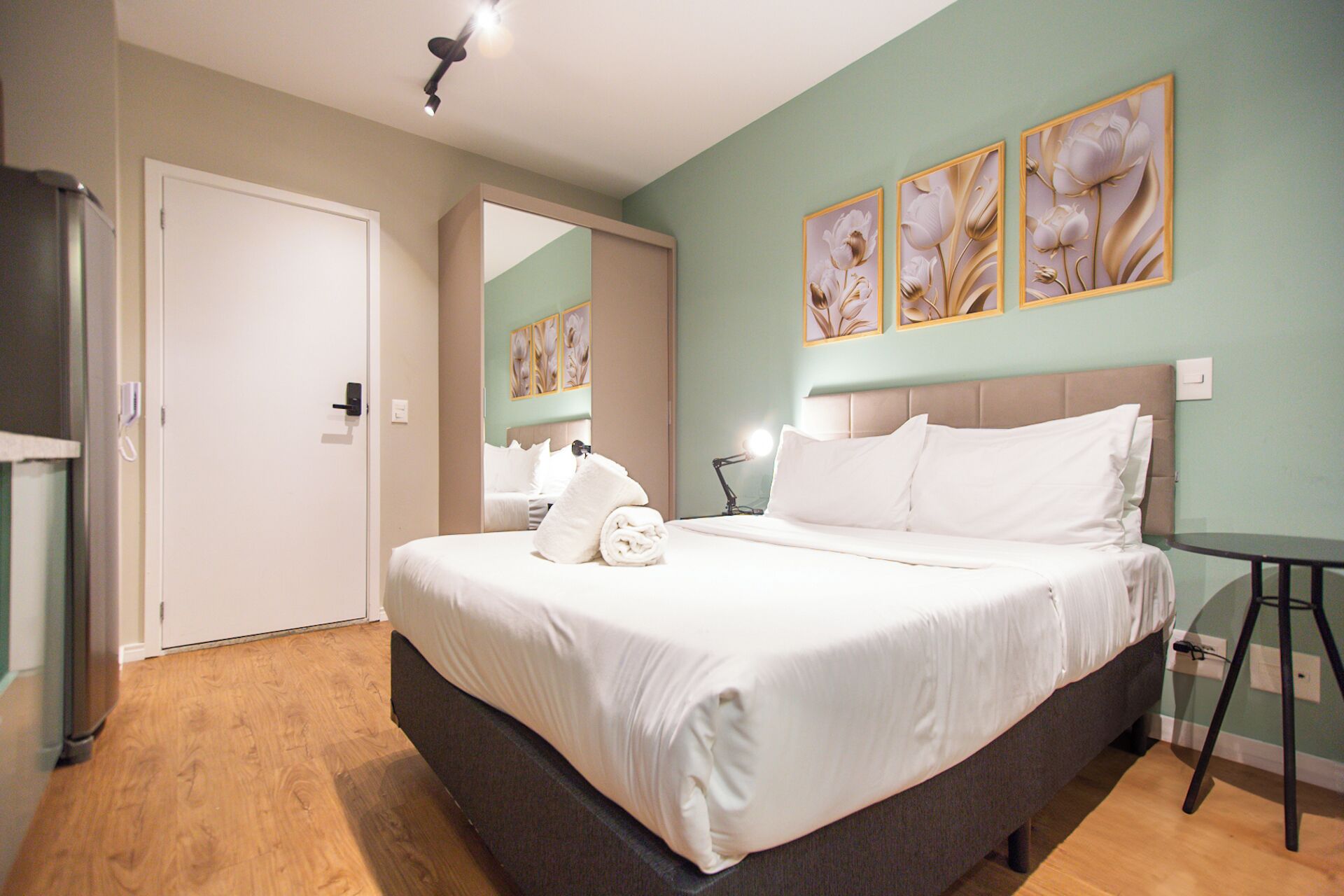 A bedroom with a bed, a bedside table, a lamp, and artwork on the wall.