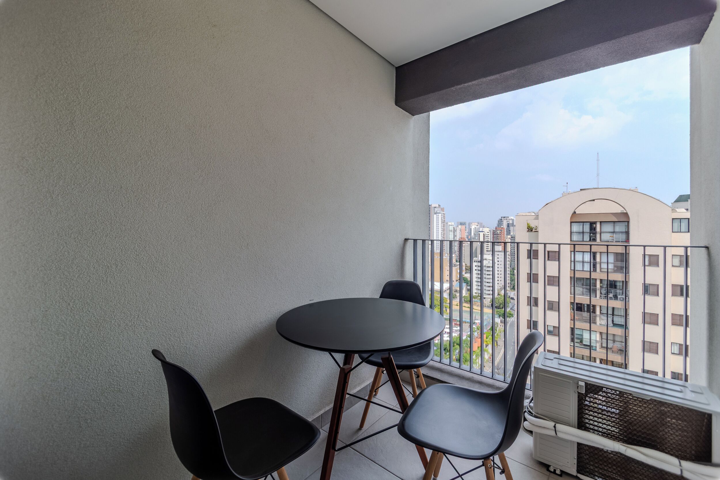 A balcony with a table and chairs, a view of the cityscape, and an air conditioning unit.