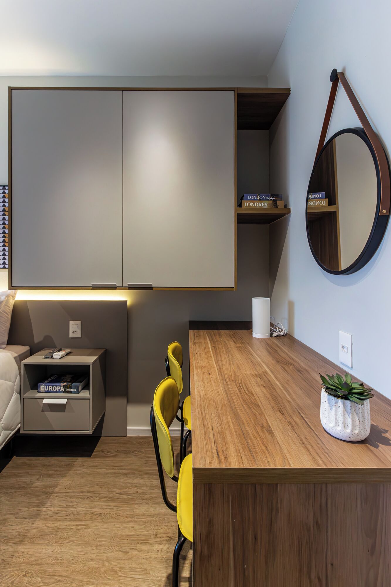 Una sala de estar moderna con una mesa de centro de madera, una silla amarilla, una mesita auxiliar con un control remoto y una estantería con libros.