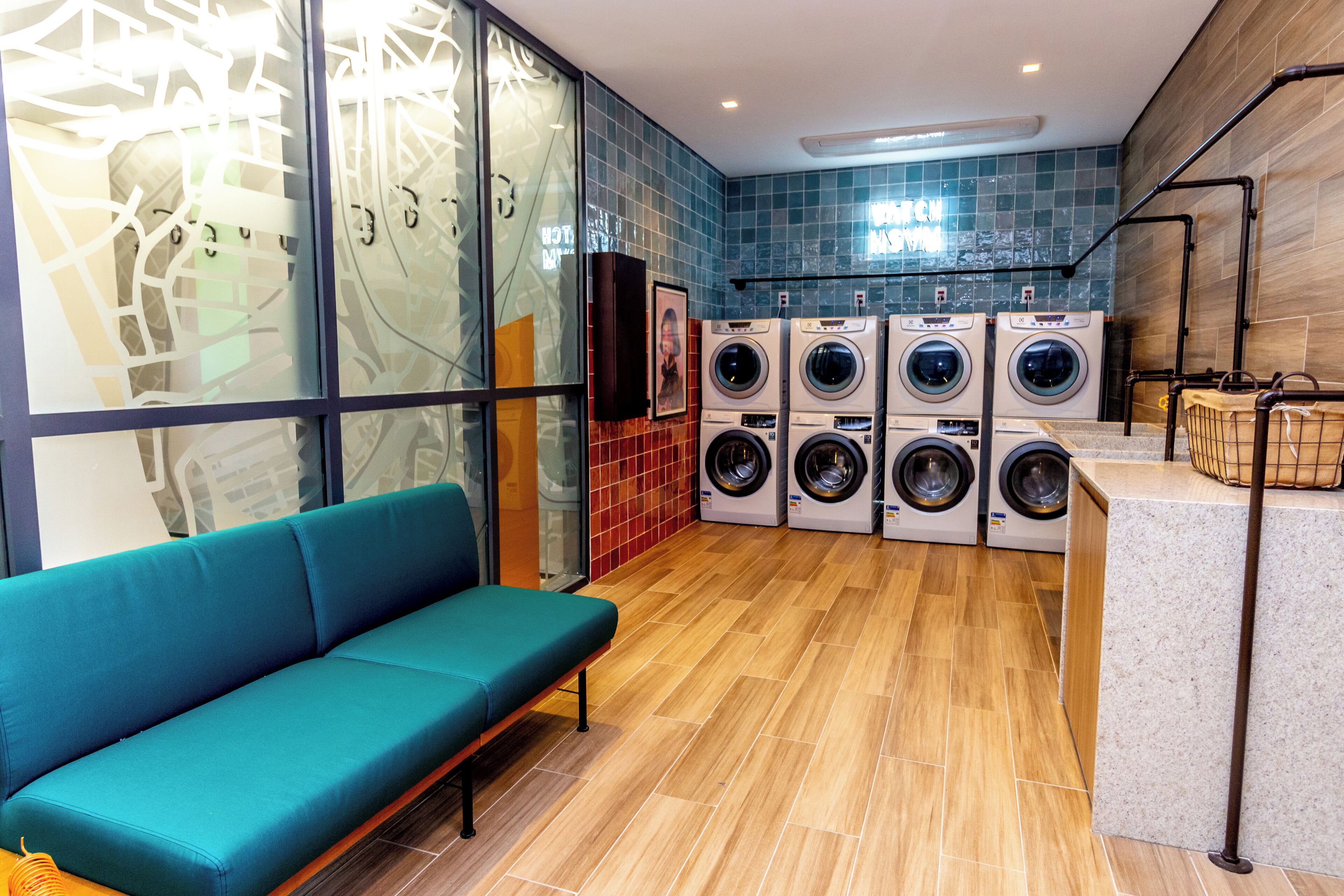 Un moderno cuarto de lavandería con un sofá color turquesa, varias lavadoras y un salpicadero de azulejos.