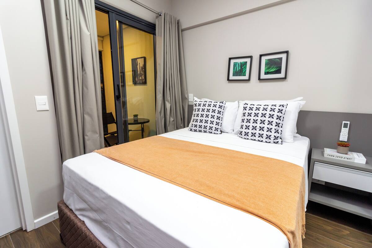 Hotellihuone, jossa on sänky, yöpöytä, jossa on puhelin, ja pieni pöytä tuolilla.