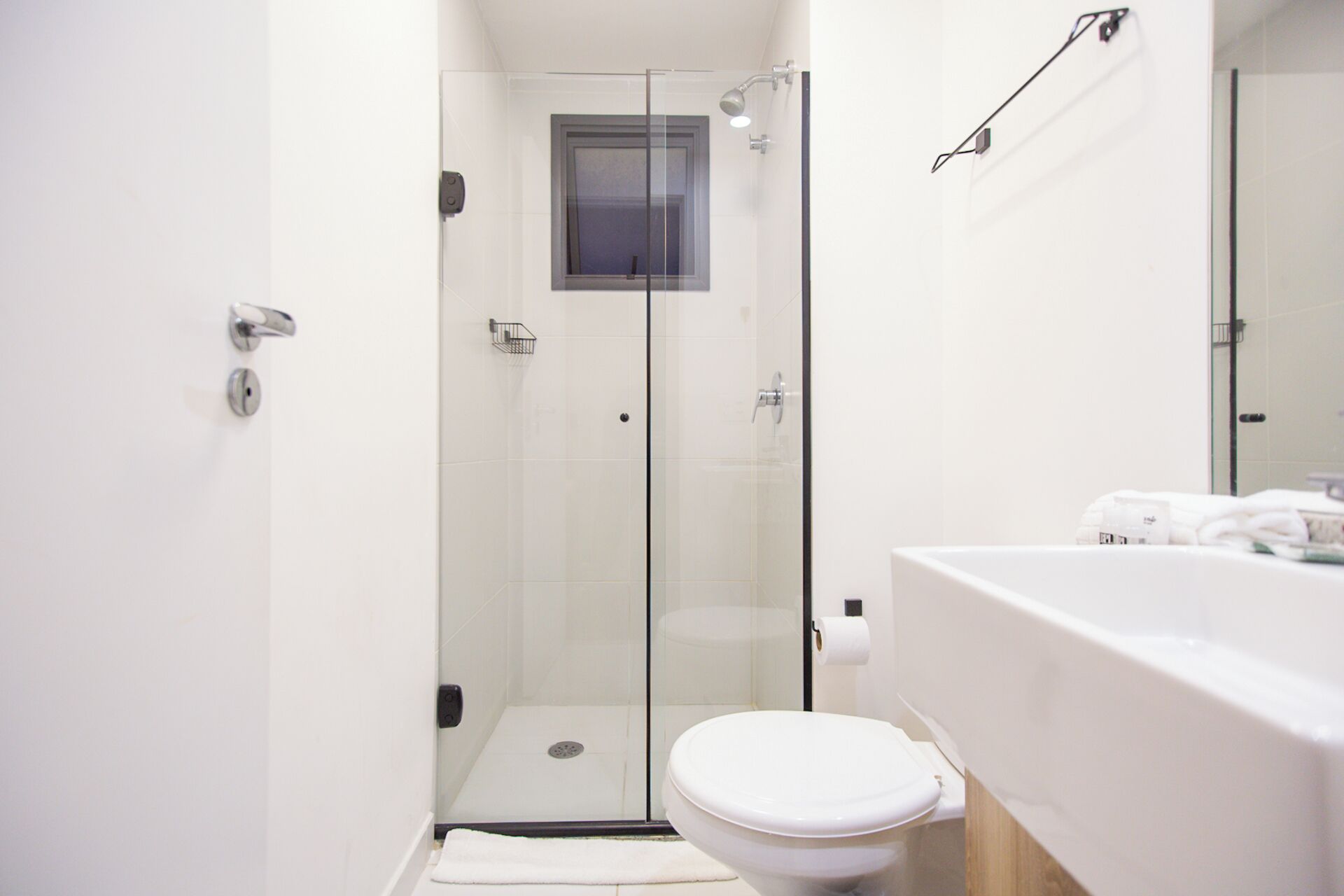 A modern bathroom with a glass-enclosed shower, a white toilet, and a white sink with a towel dispenser.