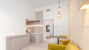 Eine moderne Küche mit integriertem Mikrowellenherd und Spüle, ein Essbereich mit einem kleinen runden Tisch und gelben Stühlen, und ein gelbes Sofa im Wohnbereich.