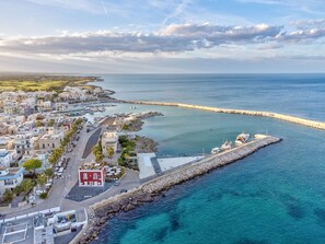 An aerial view of a coastal town with a marina, buildings, and a rocky breakwater.