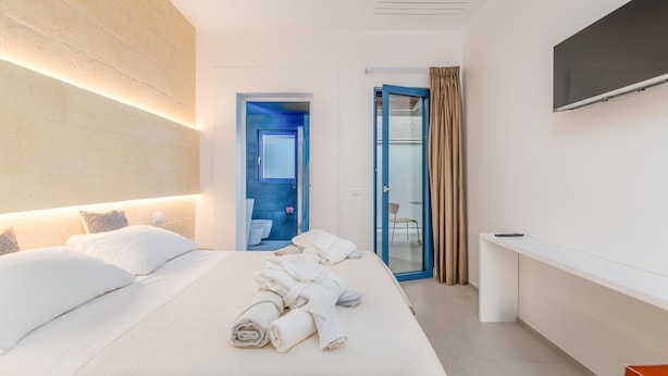 Ein modernes Hotelzimmer mit einem großen Bett, einem an der Wand montierten Fernseher und einem durchgegangene Tür erkennbaren Badezimmer.