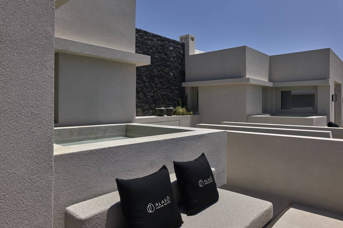 A modern outdoor terrace with a pool, stone walls, and two black cushions with the logo "ALASÓ".