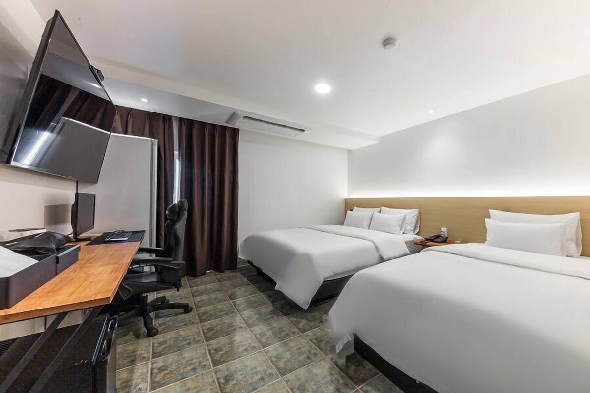 Habitación de hotel con dos camas, un escritorio con computadora, una silla y un televisor.