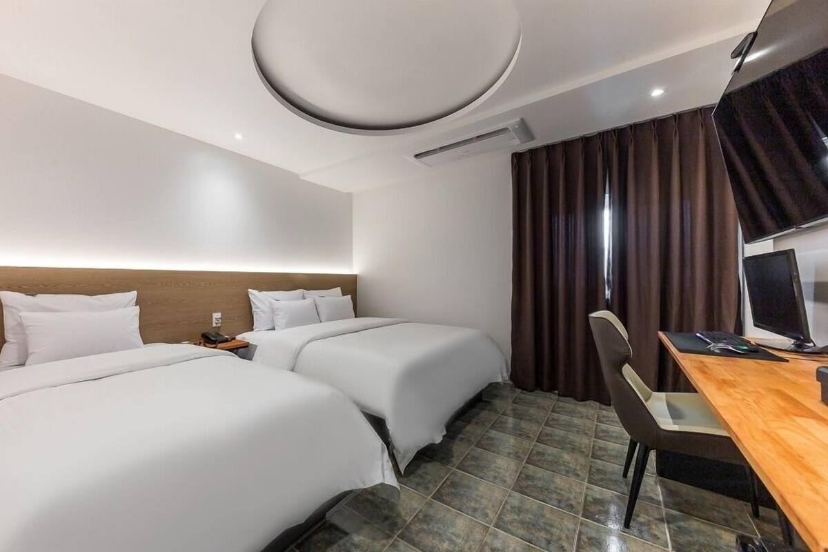 Habitación de hotel con dos camas, un escritorio con computadora y televisión.