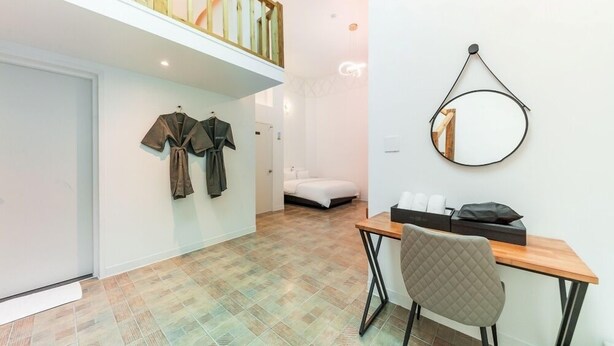 Una habitación de hotel moderna con zona de dormir en entrepiso, un pequeño escritorio con silla y un espejo montado en la pared.