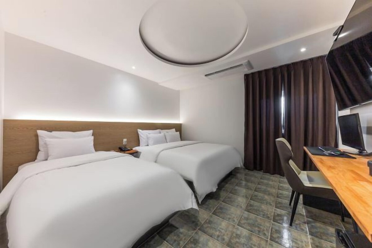A hotel room with two beds, a desk, and a chair.