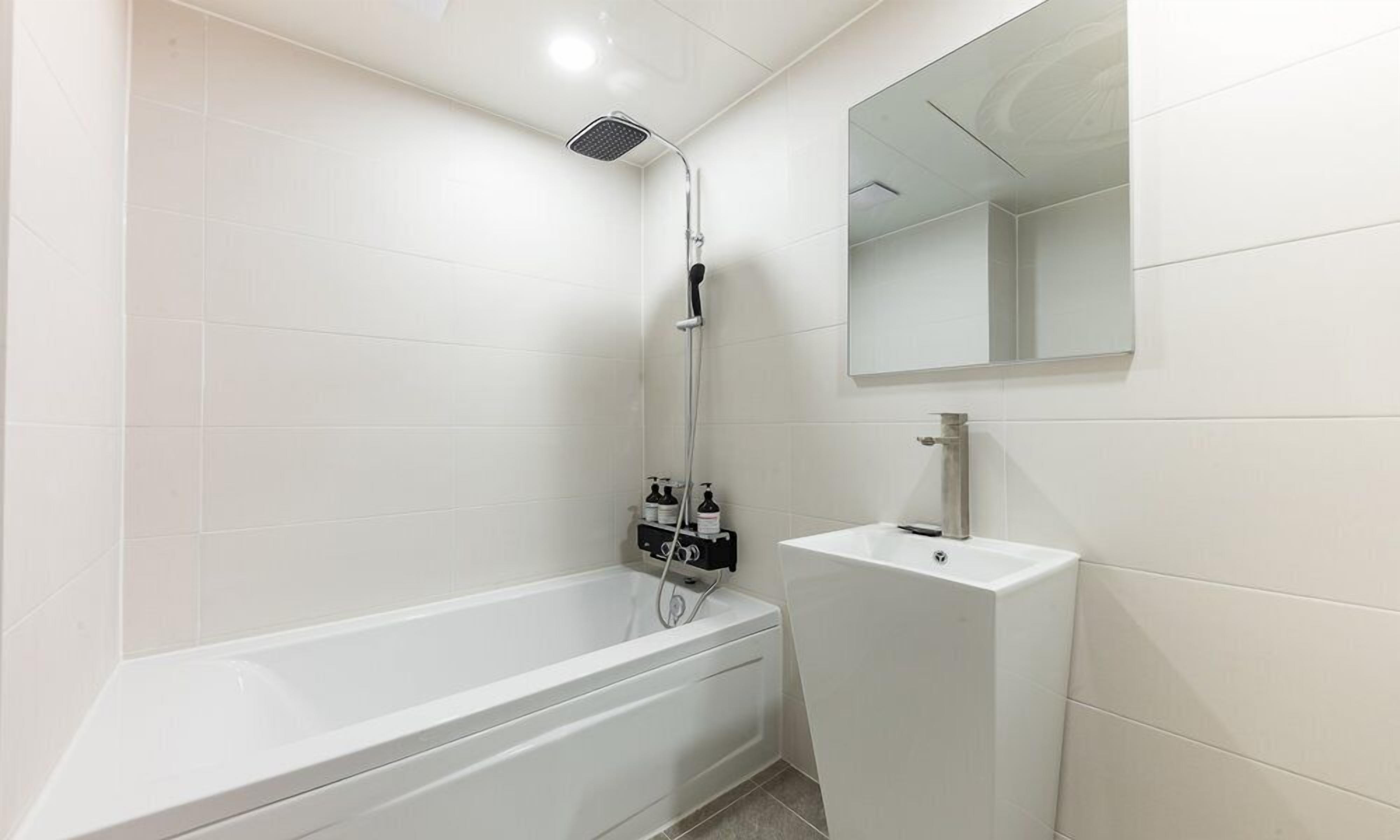 A modern bathroom with a white bathtub, a showerhead, a sink, and a mirror.