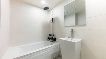 A modern bathroom with a white bathtub, a showerhead, a sink, and a mirror.