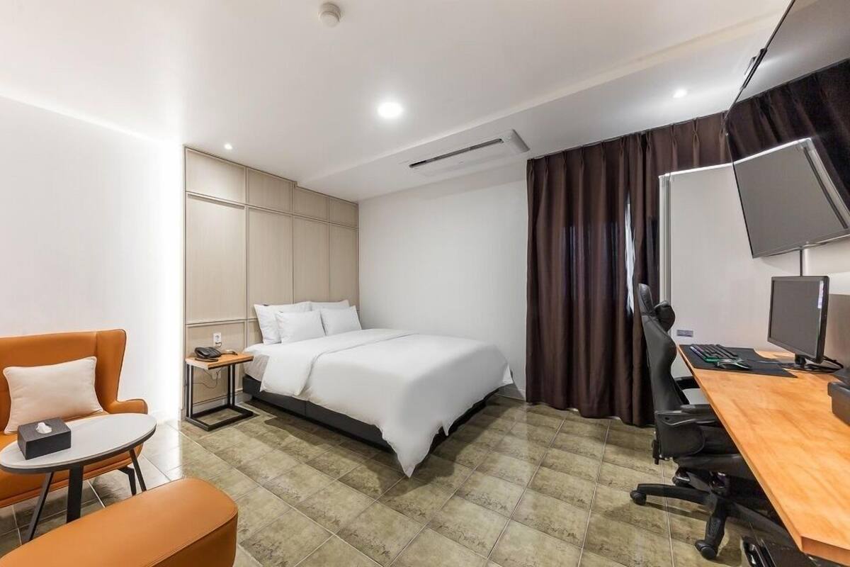 Una habitación de hotel moderna con una cama, un escritorio con computadora, una silla y una mesita.