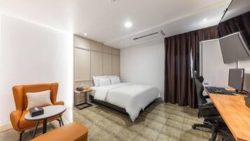 A modern hotel room with a bed, a desk with a computer, a chair, and a small table.