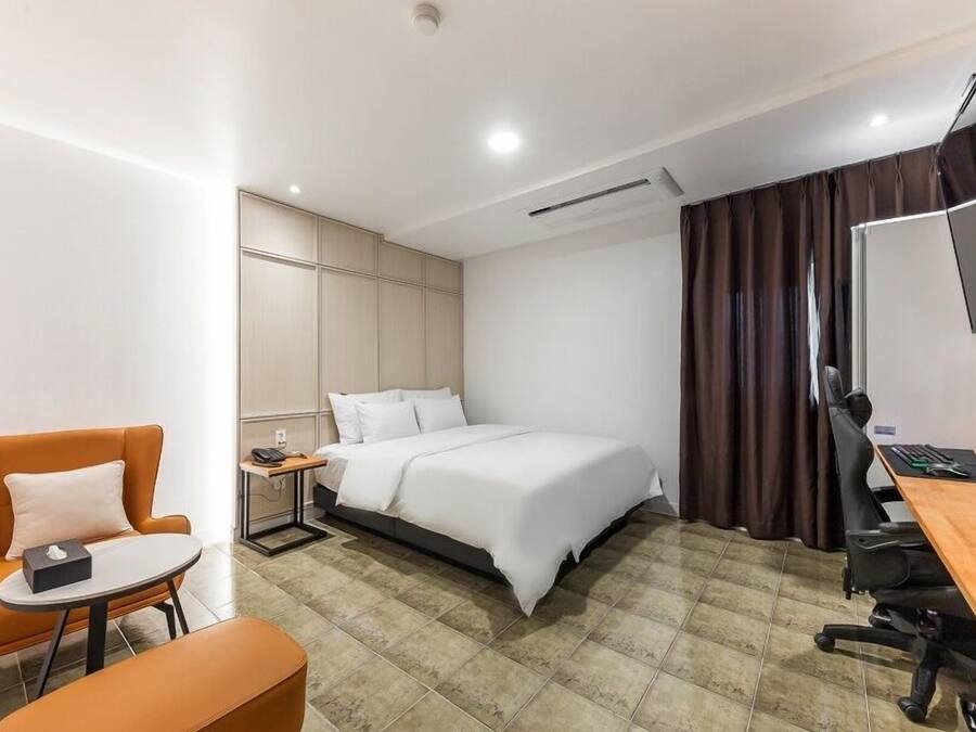 A modern hotel room with a bed, a desk with a computer, a chair, and a small table.