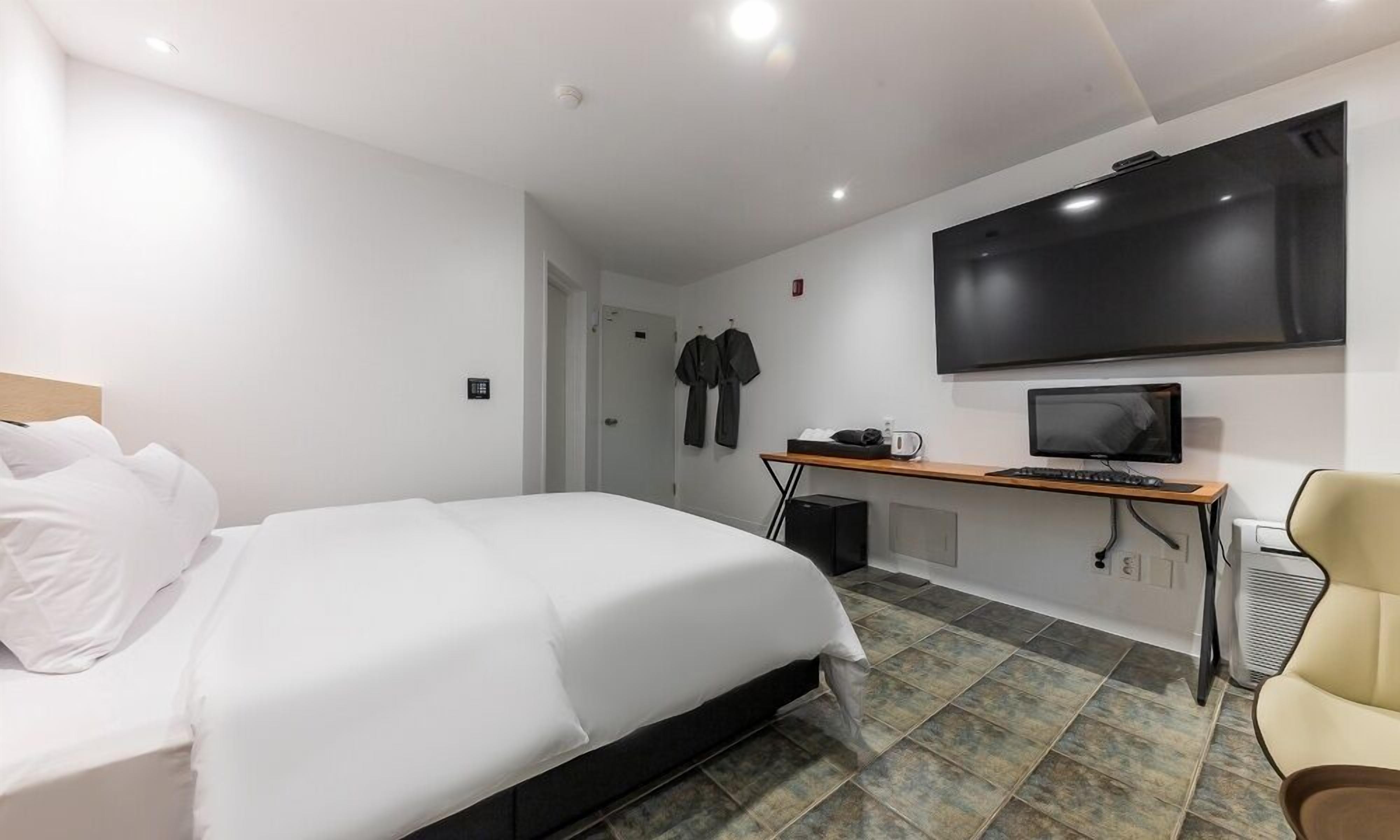 A hotel room with a bed, a desk with a computer, a TV, and a chair.