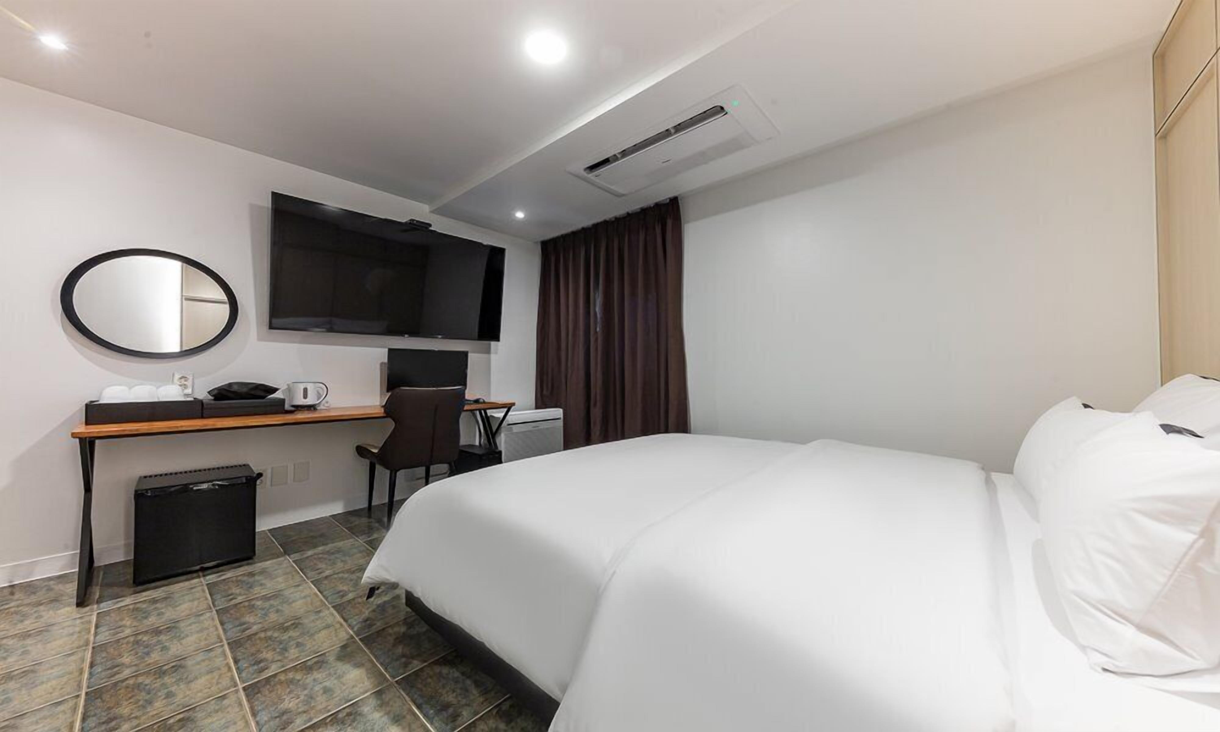 A hotel room with a bed, a desk with a chair, a television, and a small trash bin.