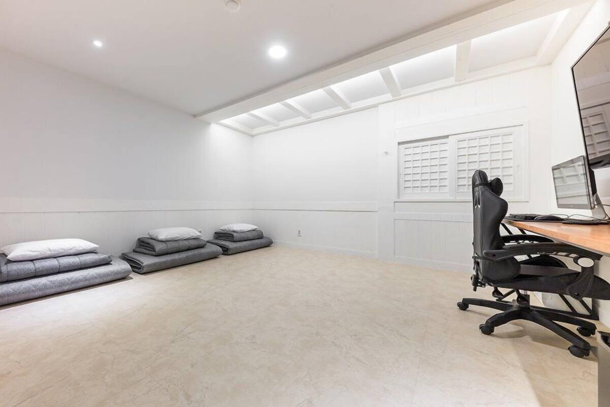 Una habitación amplia con un escritorio grande, una silla y varios colchones enrollados en el suelo.