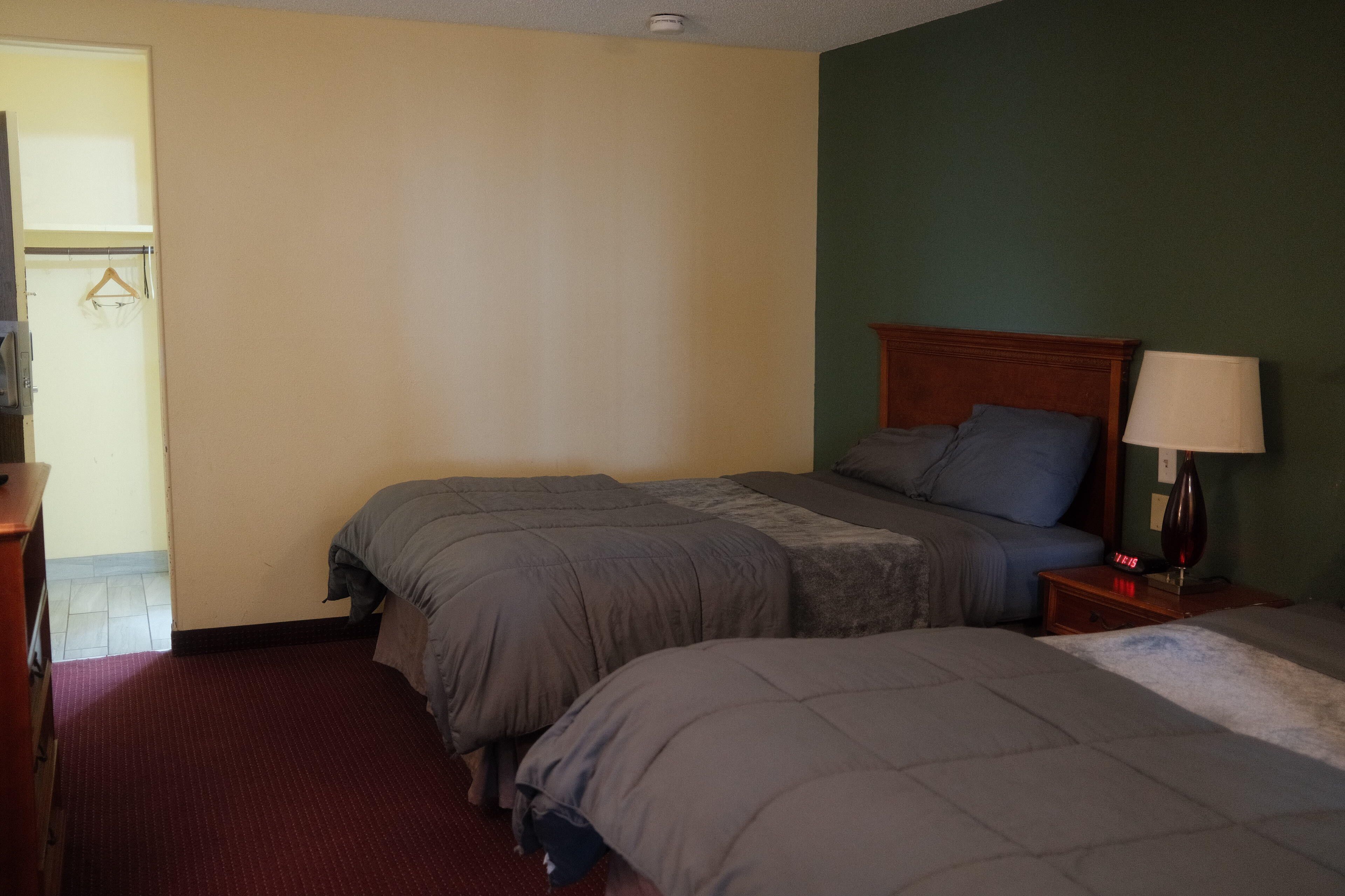A hotel room with two beds, a wooden headboard, a nightstand with a lamp, and a red carpet.