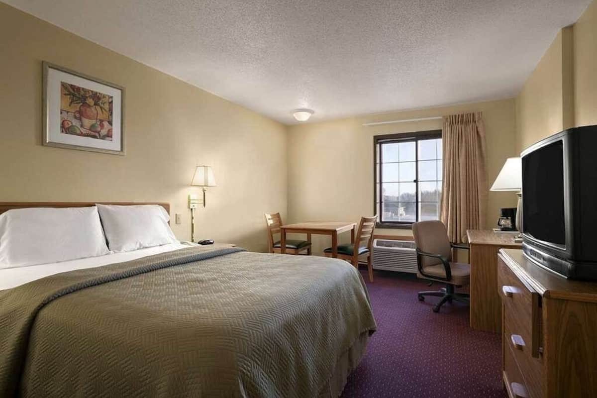 Una habitación de hotel con cama, escritorio, silla, televisión y ventana.