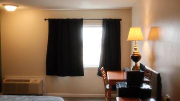 A hotel room with a bed, a desk, a chair, a lamp, and a window with curtains.