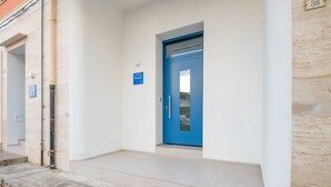 Entrada de edificio con puerta azul, una ventana pequeña y un letrero que indica zona de estacionamiento.