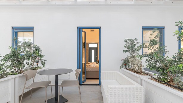 Un pequeño patio amurallado con una mesa redonda y sillas, un sofá blanco y plantas en macetas.