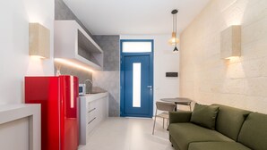 Una cocina compacta con un refrigerador rojo, armarios blancos y una puerta azul.