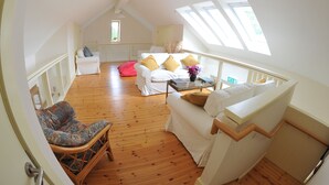A spacious loft bedroom with a high ceiling, wooden flooring, a white sofa, a wicker chair, and a small table with a vase of flowers. - Blackstairs Shepherds Huts (Knocksquire)