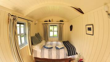 A cozy bedroom with a bed, curtains, a window, a wall-mounted light, and a framed picture.