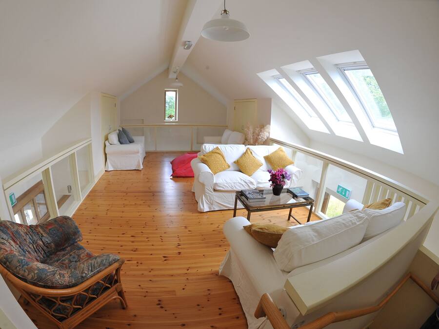 A spacious loft bedroom with a sloped ceiling, wooden flooring, and large windows.
