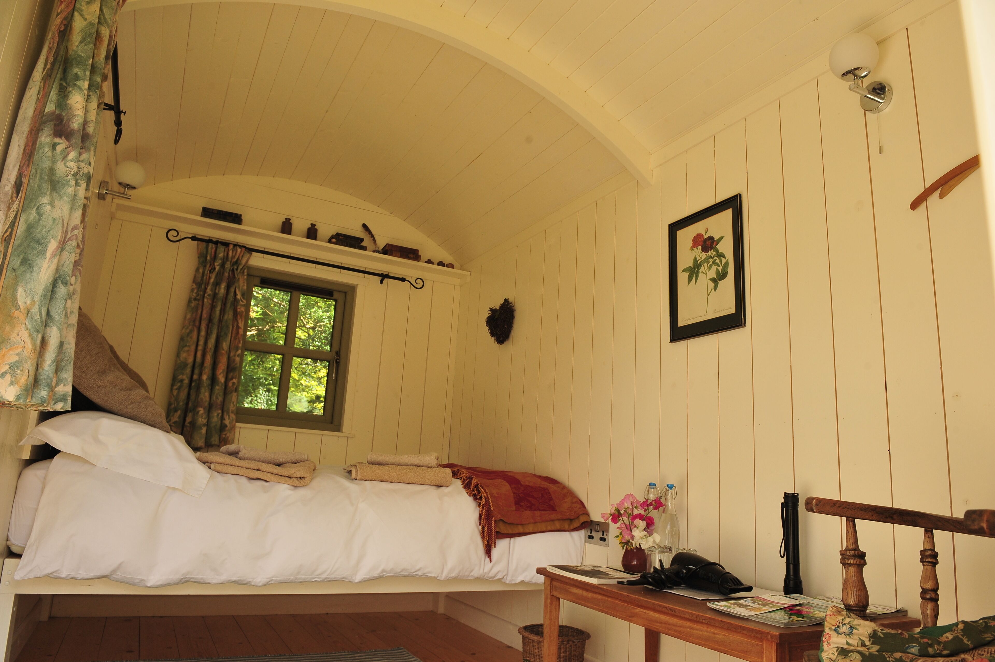 Ein gemütliches Schlafzimmer mit Bett, Fenster, Nachttisch mit Lampe und einem gerahmten Bild an der Wand.