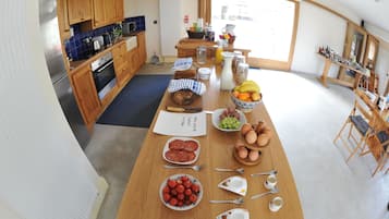 Een keuken met houten kastjes, een koelkast en een ontbijtgedeekte eettafel.