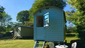 A small, light blue mobile home with a door open, a ladder leading to the entrance, and a table with two chairs outside. - Blackstairs Shepherds Huts (Knocksquire)