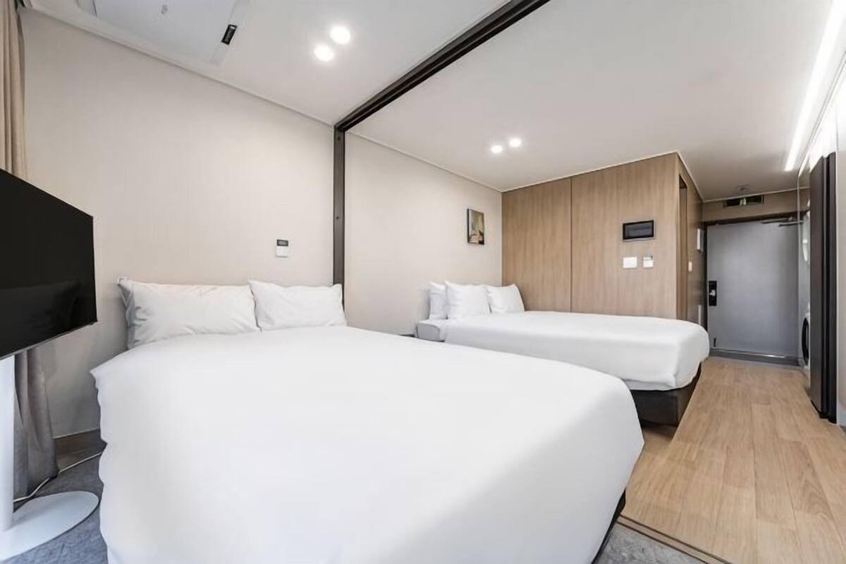 A hotel room with two beds, a flat-screen TV, a wooden panel wall, and a door leading to a bathroom.