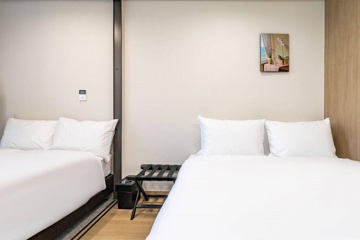 A hotel room with two single beds, a small table, and a wall-mounted artwork.