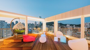 A rooftop lounge with a wooden deck, hanging chairs, and a city view.