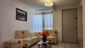 A living room with a sofa set, a small table with a vase of flowers, a painting on the wall, and a door. - Cuernavaca (Emiliano Zapata)