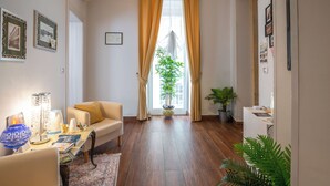 Ein Wohnzimmer mit einer Couch, einem Couchtisch mit Lampe, einer Zimmerpflanze und Blick auf ein Gebäude durch ein Fenster mit Vorhängen.