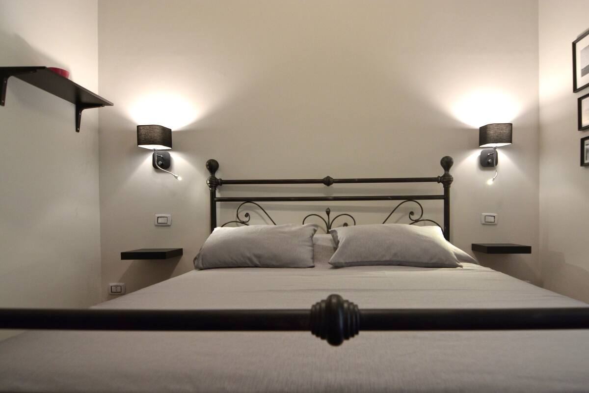Een slaapkamer met een bed, twee bedlampen, een wandplank en een spiegel.