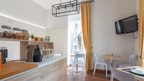 Eine moderne Küche mit Kaffeemaschine, Vorratseimern und einer Holzauskładung. Ein Essbereich mit weißen Stühlen und einem Tisch, sowie ein an der Wand befestigter Fernseher.