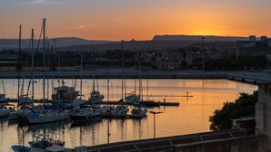 Ein Yachthafen mit mehreren anglegerten Booten, eine Brücke im Hintergrund und ein Sonnenuntergang über dem Wasser.