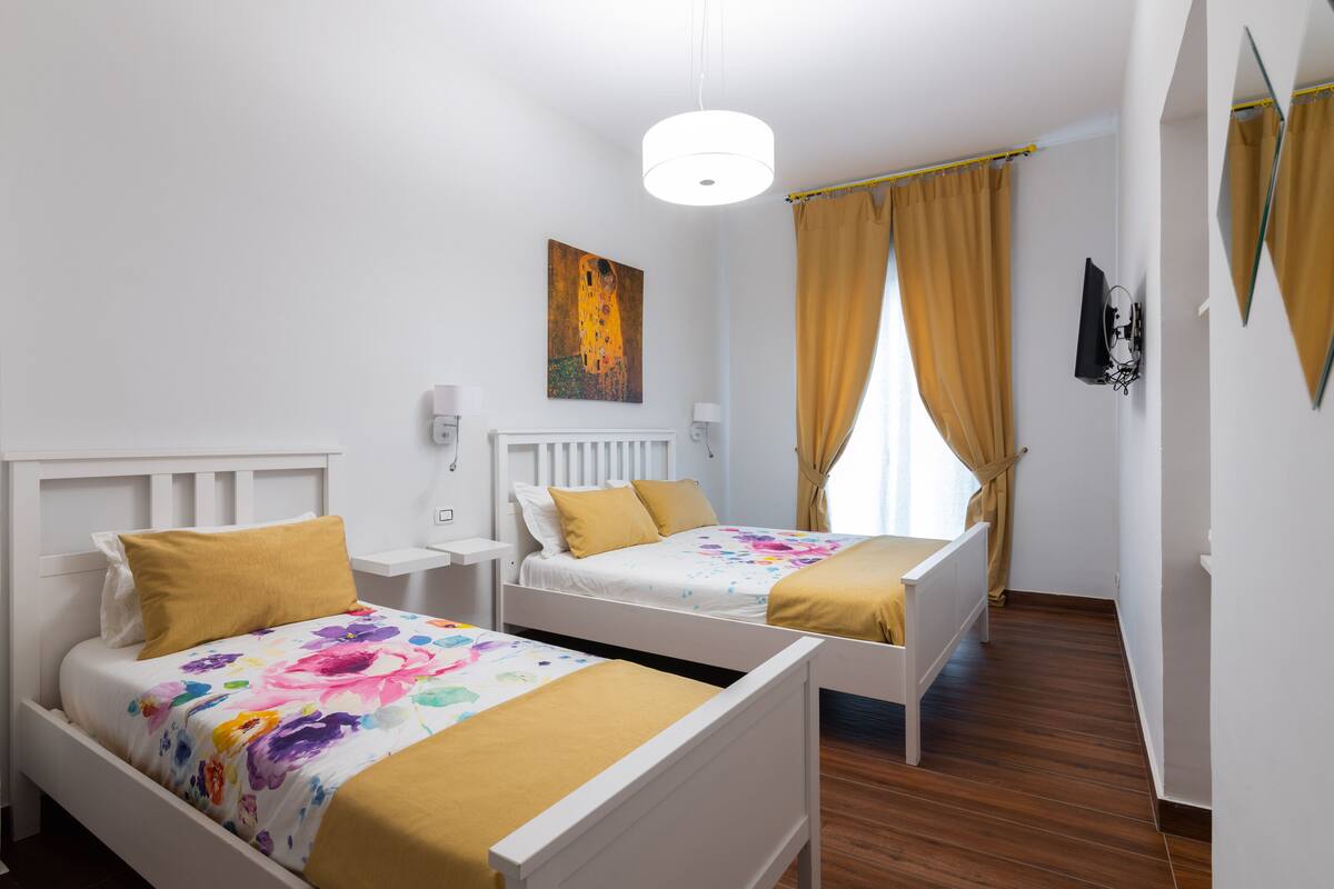 Een hotelkamer met twee enkele bedden, een witte radiator, een schilderij aan de muur en een raam met gordijnen.