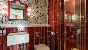 Une salle de bain avec un mur recouvert de carreaux rouges, un lavabo blanc, des toilettes, une douche et un miroir avec un cadre rouge.