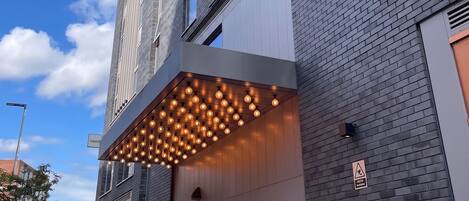 Un edificio moderno con fachada de ladrillo, un acceso cubierto con luces colgantes y un letrero que anuncia eventos de música en vivo.