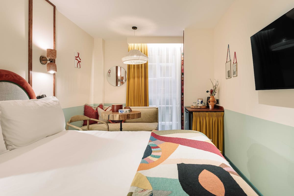 Habitación de hotel con una cama grande, un sofá, una mesita con lámpara y un televisor montado en la pared.