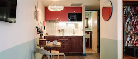 Una habitación de hotel compacta con kitchenette, un comedor con mesa y sillas, y una cama con colcha de colores.