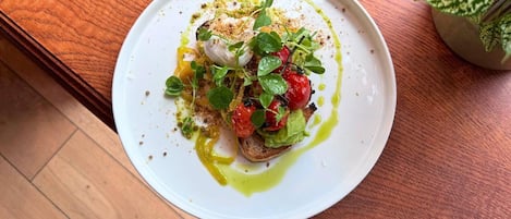 Un plato blanco con una porción de bruschetta cubierta de tomates, verduras y un chorrito de aceite de oliva.